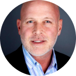 headshot of Ryan Burns, wearing a suit coat and blue striped button up